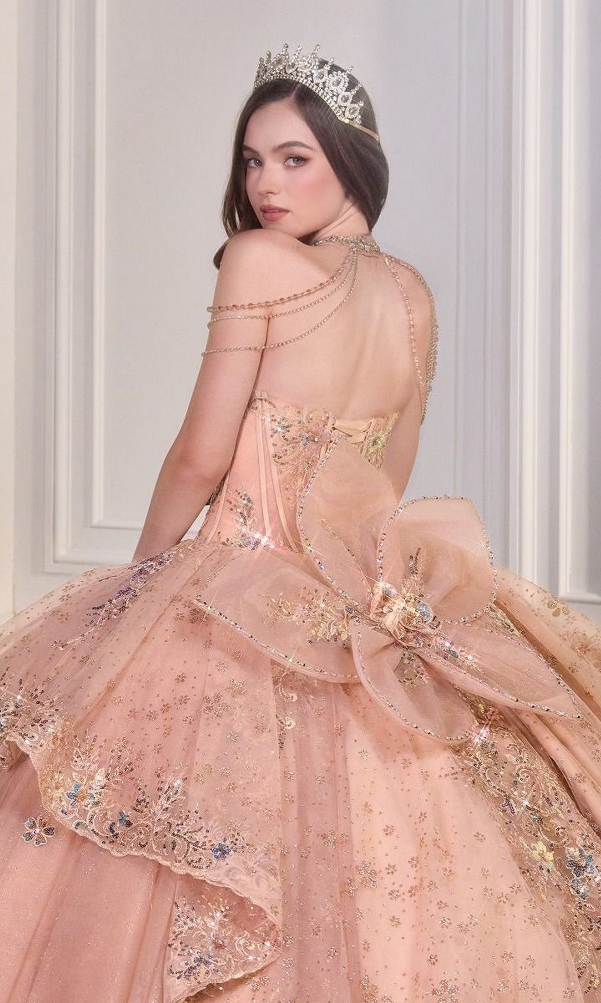 A young woman in the Quinceanera Dress 15727 By Ladivine, featuring rose gold beaded embroidery and a jeweled tiara, poses against an elegant, light-toned backdrop.